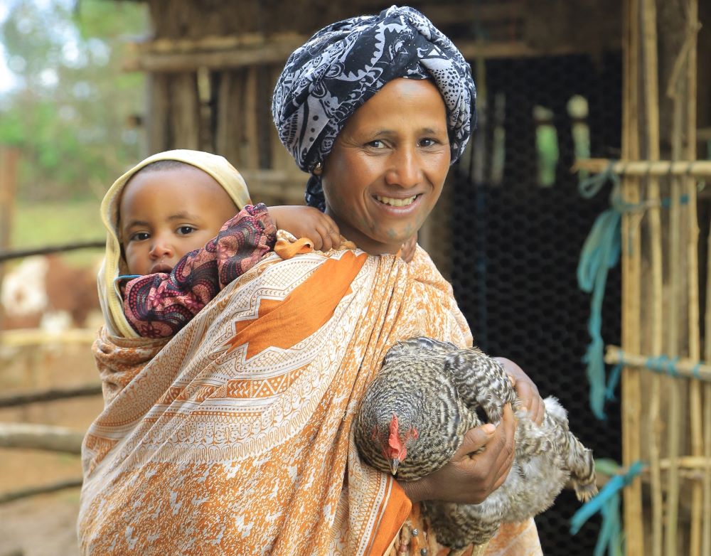Zuribet - Nutrition International A mother has her baby on her back while she holds a chicken