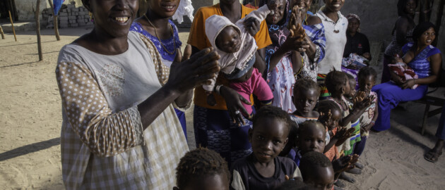 group of clapping women and children holding baby seated woman breastfeeding in background