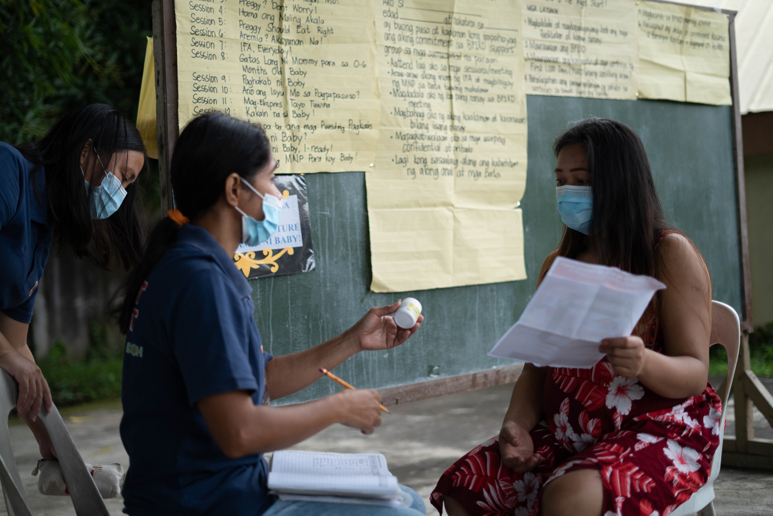Philippines_BF1KD_DSC0480 - Nutrition International Community health volunteers speaks to a mother outside and both are wearing masks.