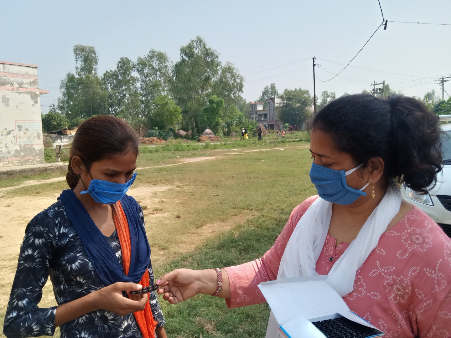 - Nutrition International A principal in India stands to the right of a student and hands her a package of iron and folic acid supplements.