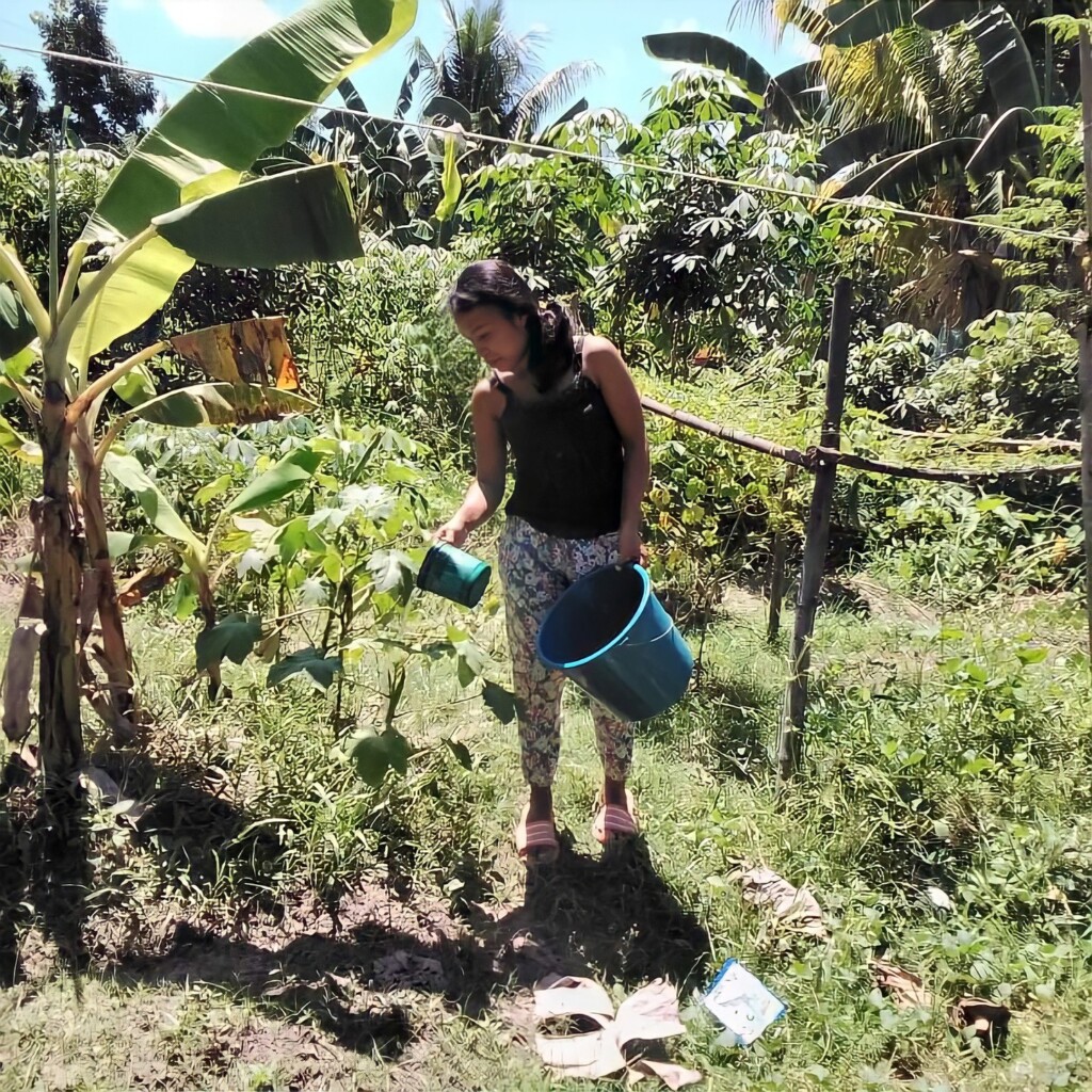 Backyard gardening (3) - Nutrition International Woman standing outside watering her garden in the Philippines