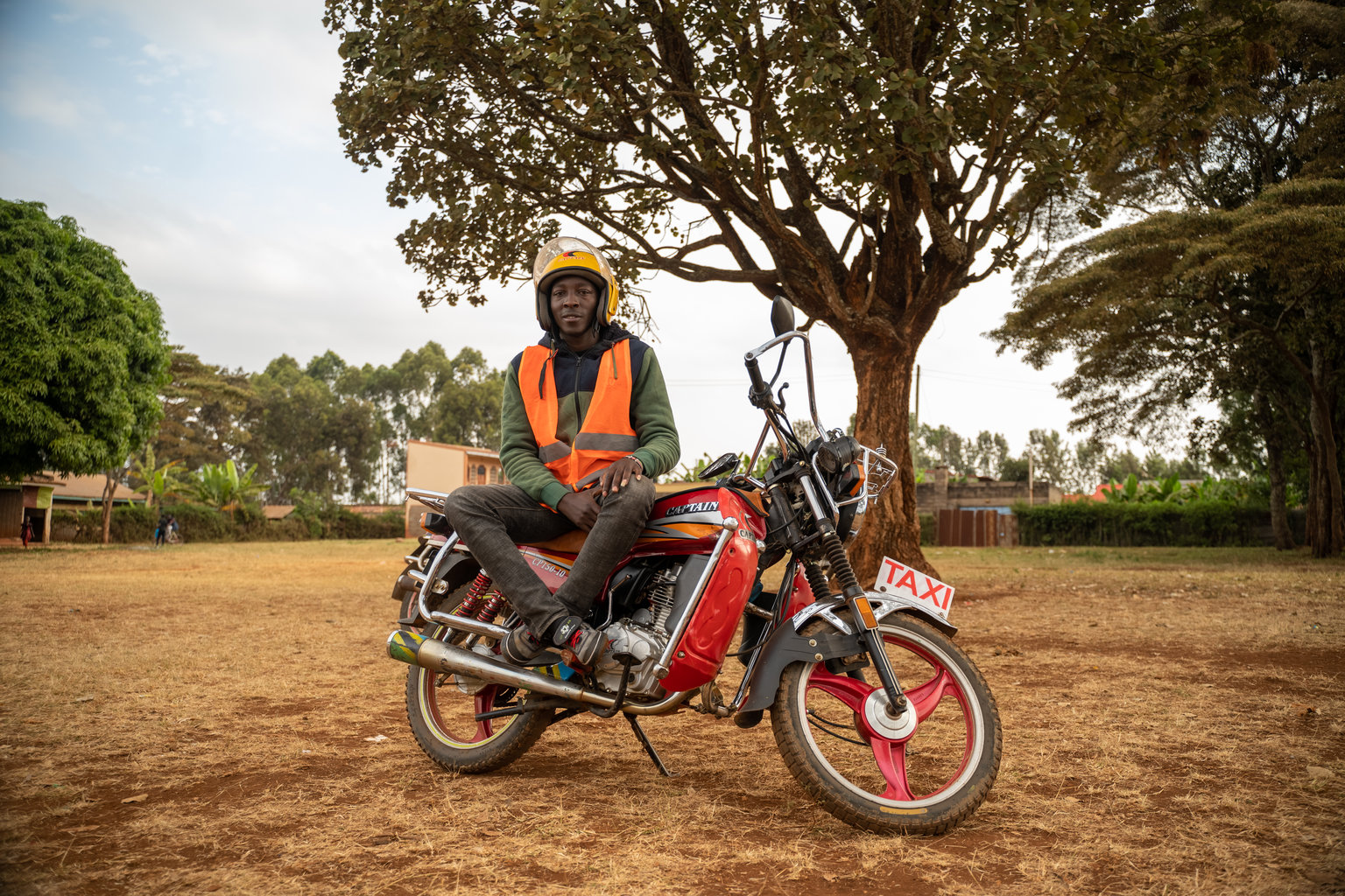 DSC00394 - Nutrition International A man in an orange vest wears his helmet sitting on top of a motorcycle that he drives as a taxi service.
