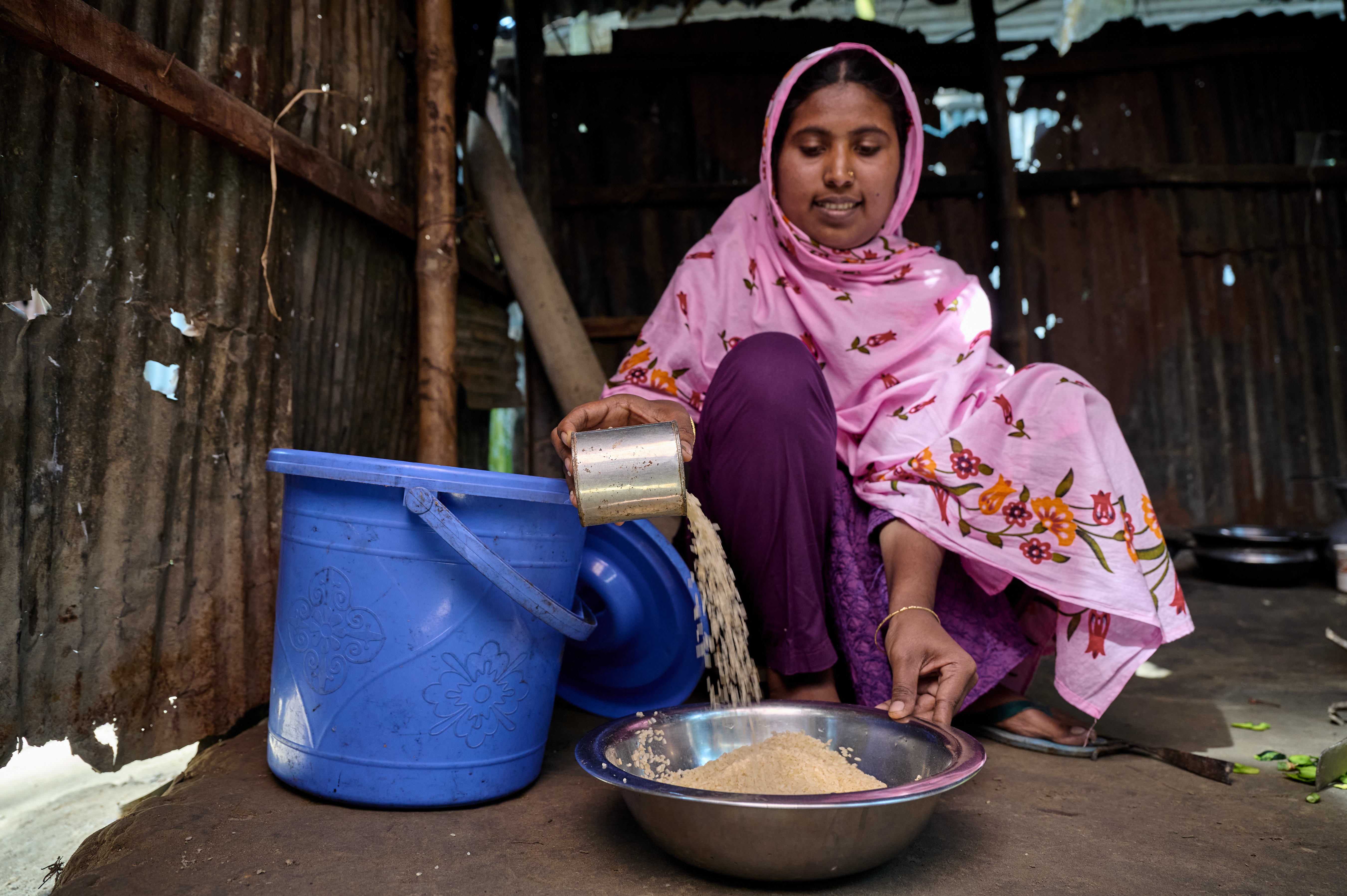 0120-NI-BD-21-11-2022-sujanmap - Nutrition International A woman measure rices by pouring it into a bowl. The kernals are a cascading waterfall and build up a mound.