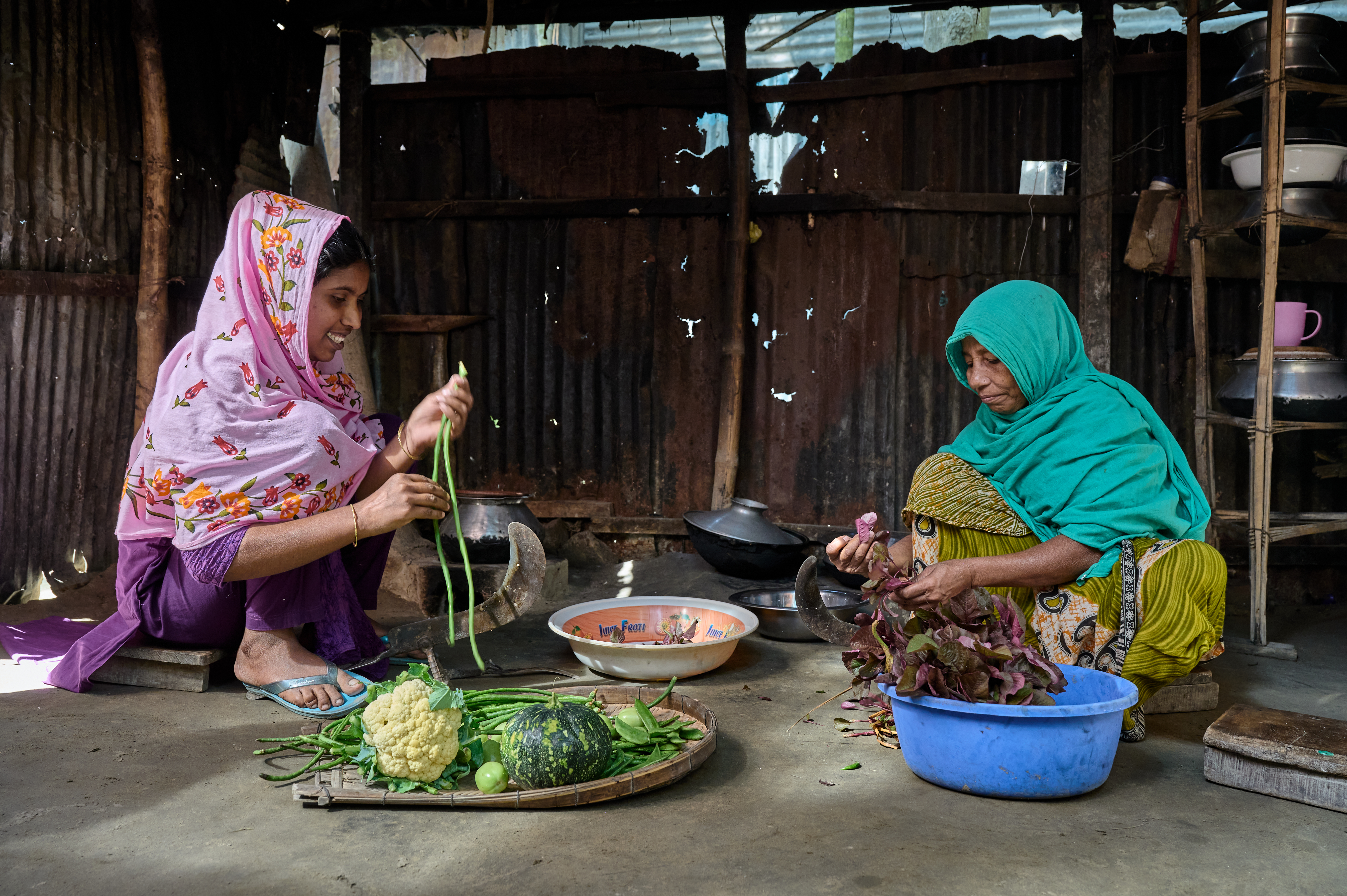 0127-NI-BD-21-11-2022-sujanmap - Nutrition International Two women prepare the midday meal together. Rice is the common base for meals, and they are preparing vegetable curry to accompany it.