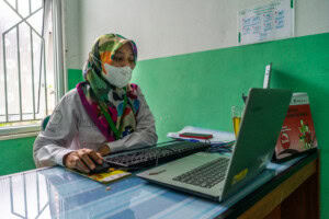 2023_02_01_Indonesia_Maternal Health_Puskesmas_Wawan Buditjahjono (14) - Nutrition International Tita Rosita sitting at desk using laptop